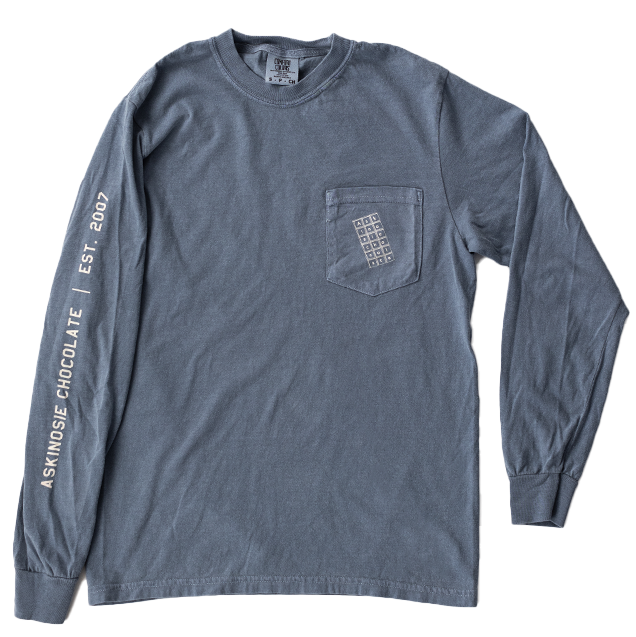 Blue-grey long-sleeve shirt with a chocolate bar on the pocket and Askinosie Chocoalte text on sleeve against a white background